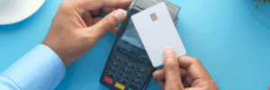 A person holds a white credit card over a payment terminal, ready to tap for a transaction. The image illustrates electronic payment processing, relevant to understanding effective rates for credit card transactions.