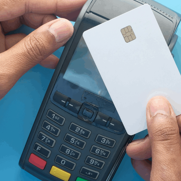 A person holds a white credit card over a payment terminal, ready to tap for a transaction. The image illustrates electronic payment processing, relevant to understanding effective rates for credit card transactions.