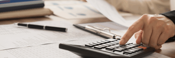 A hand using a calculator while reviewing financial statements, symbolizing veterinary practice bookkeeping and P&L analysis.